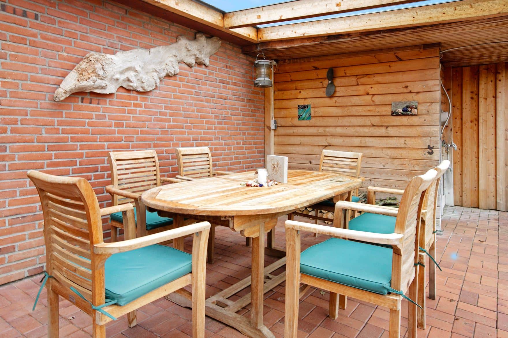 The covered walk along the brick wall with an oval teak table and six chairs, a whalebone on the wall and timber cladding to the right.