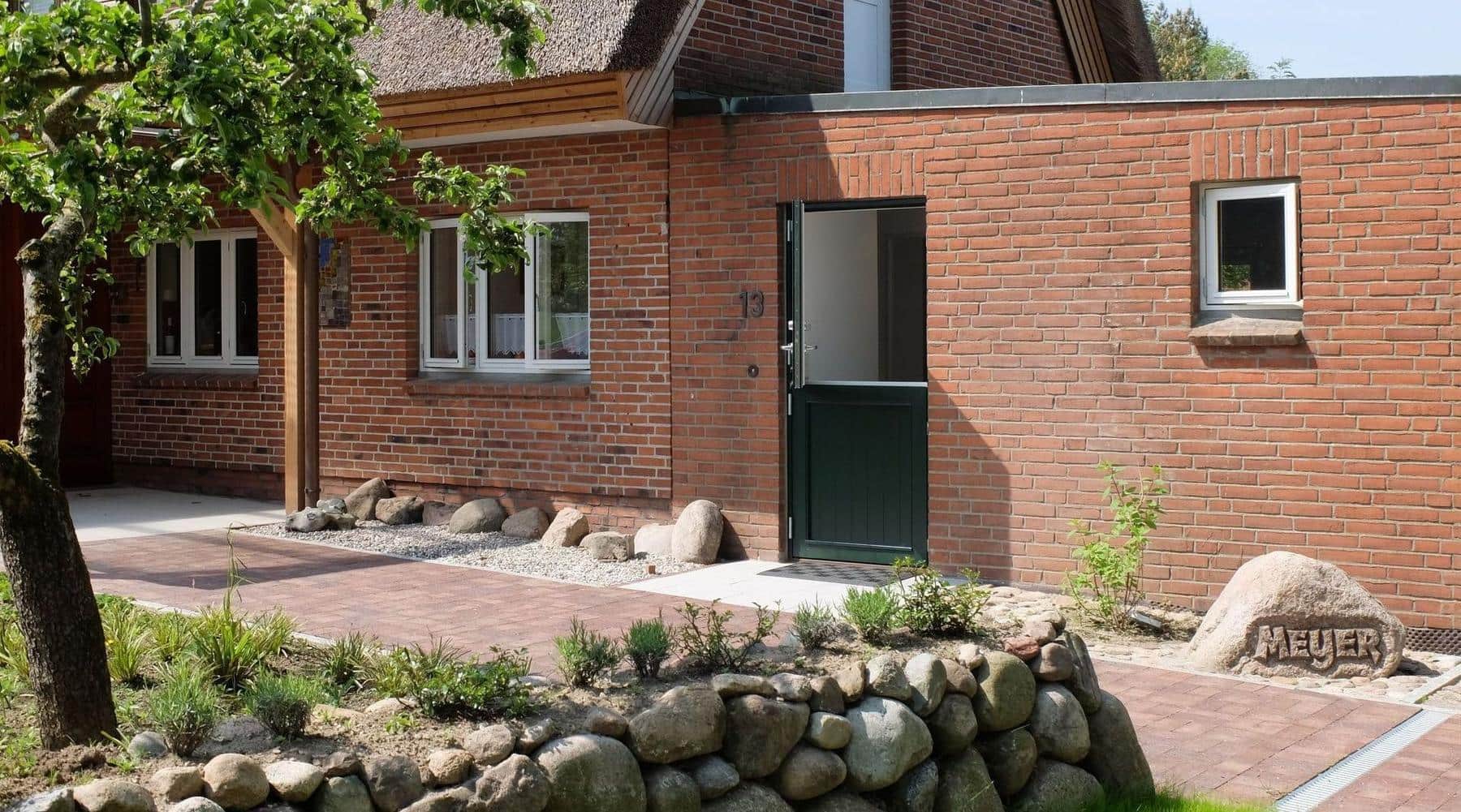 A brick facade with the green stable door standing open at the top; to the right a boulder with the name Meyer carved into it.