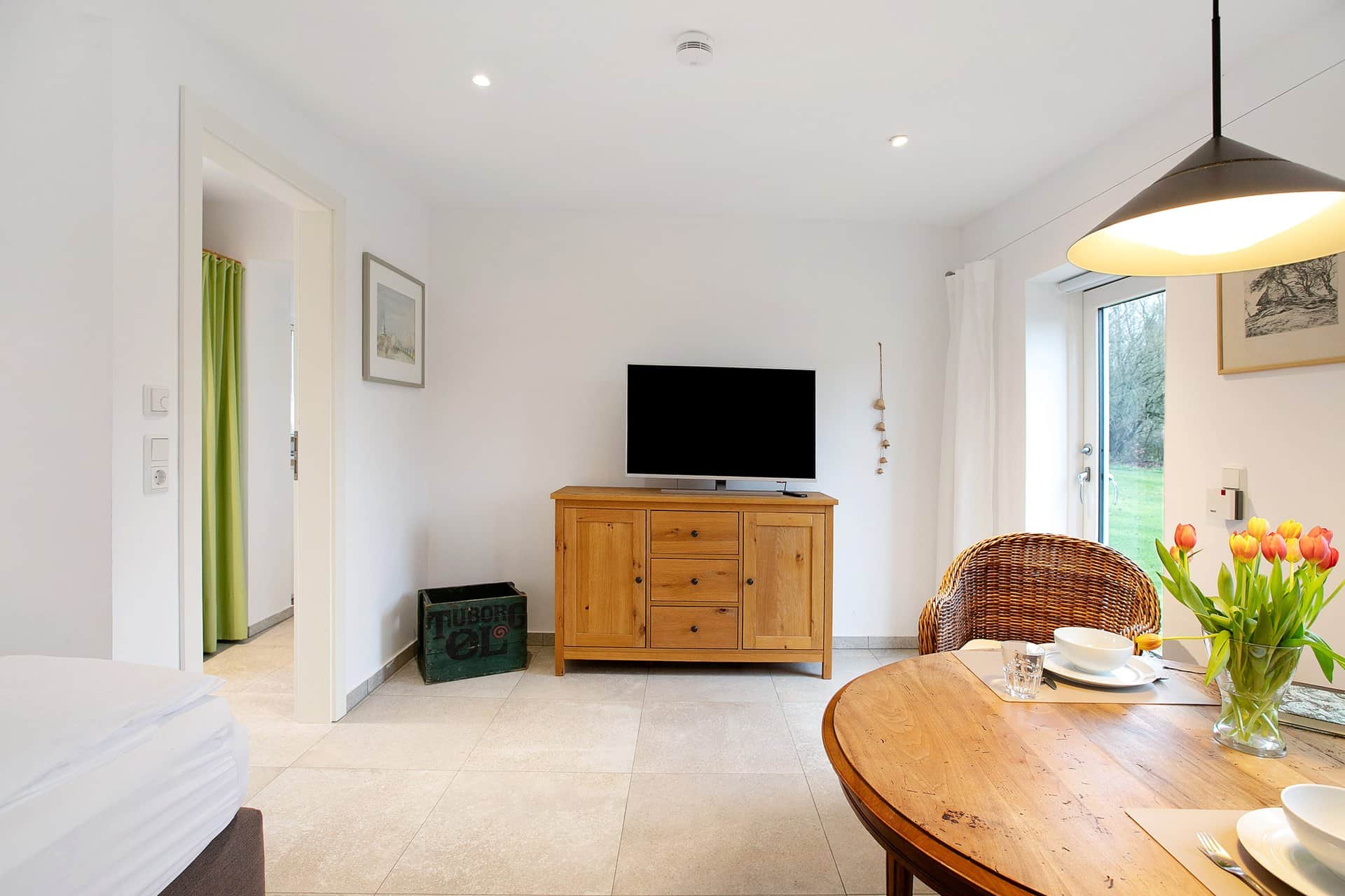 The living and sleeping room in one: the foot of the bed on the left, a chest of drawers with a television in the middle and the round table with tulips on the right.