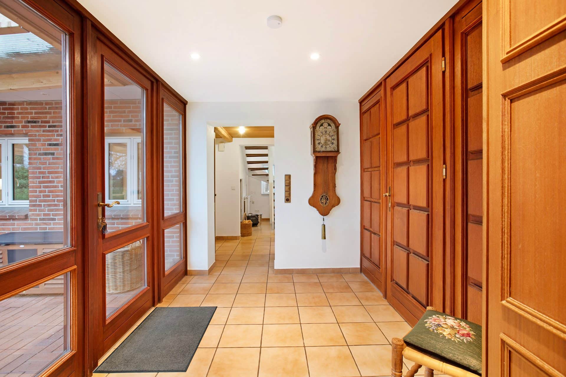The hallway between glazed doors: full-height wood panelling with an old pendulum clock on the wall and a view through to the staircase.