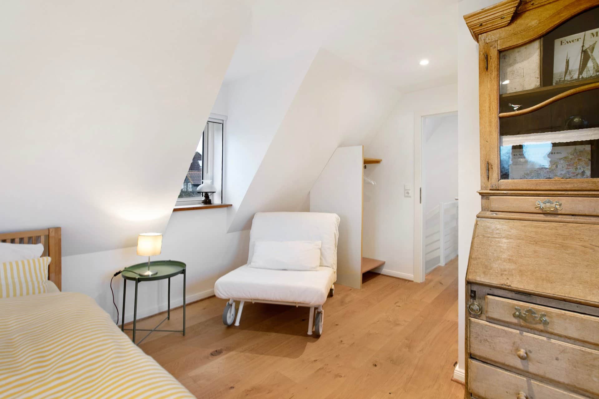 The foot of the second bed, with a white sleeper chair on castors folded out beside it and a side table under the dormer window.