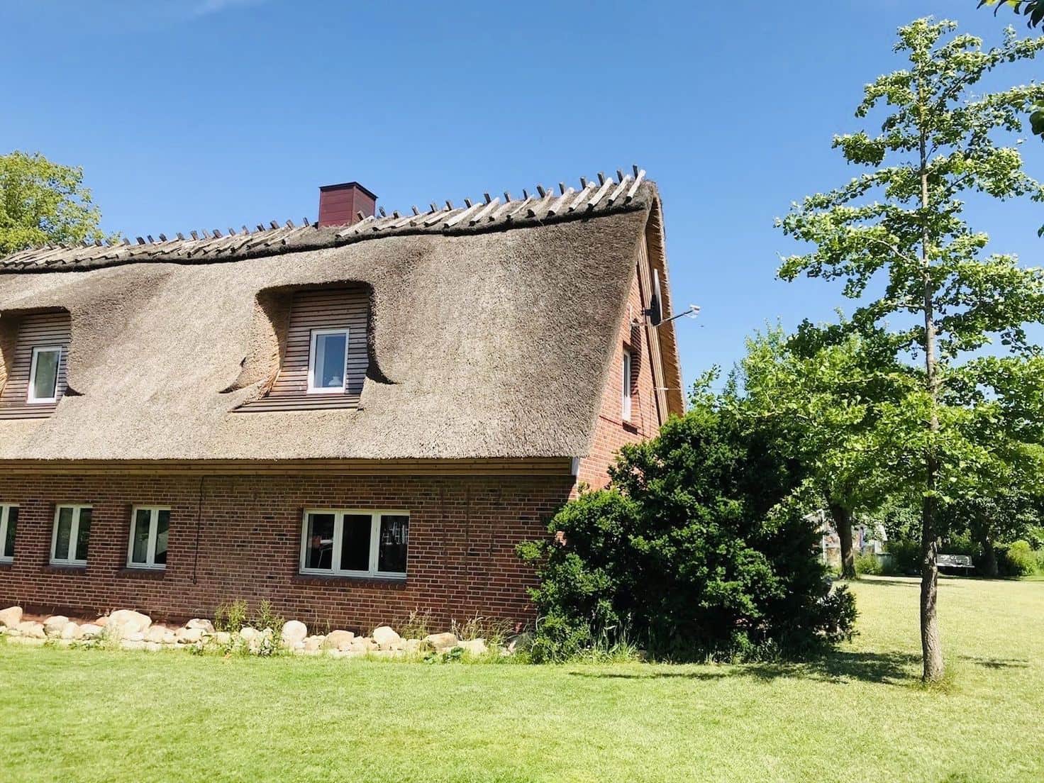 Gable end of the thatched house with a dormer curving into the reed, a red brick wall and fieldstones along the base.